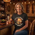 Woman sitting at a bar wearing a t-shirt with a beach and bourbon design, holding a glass of bourbon.