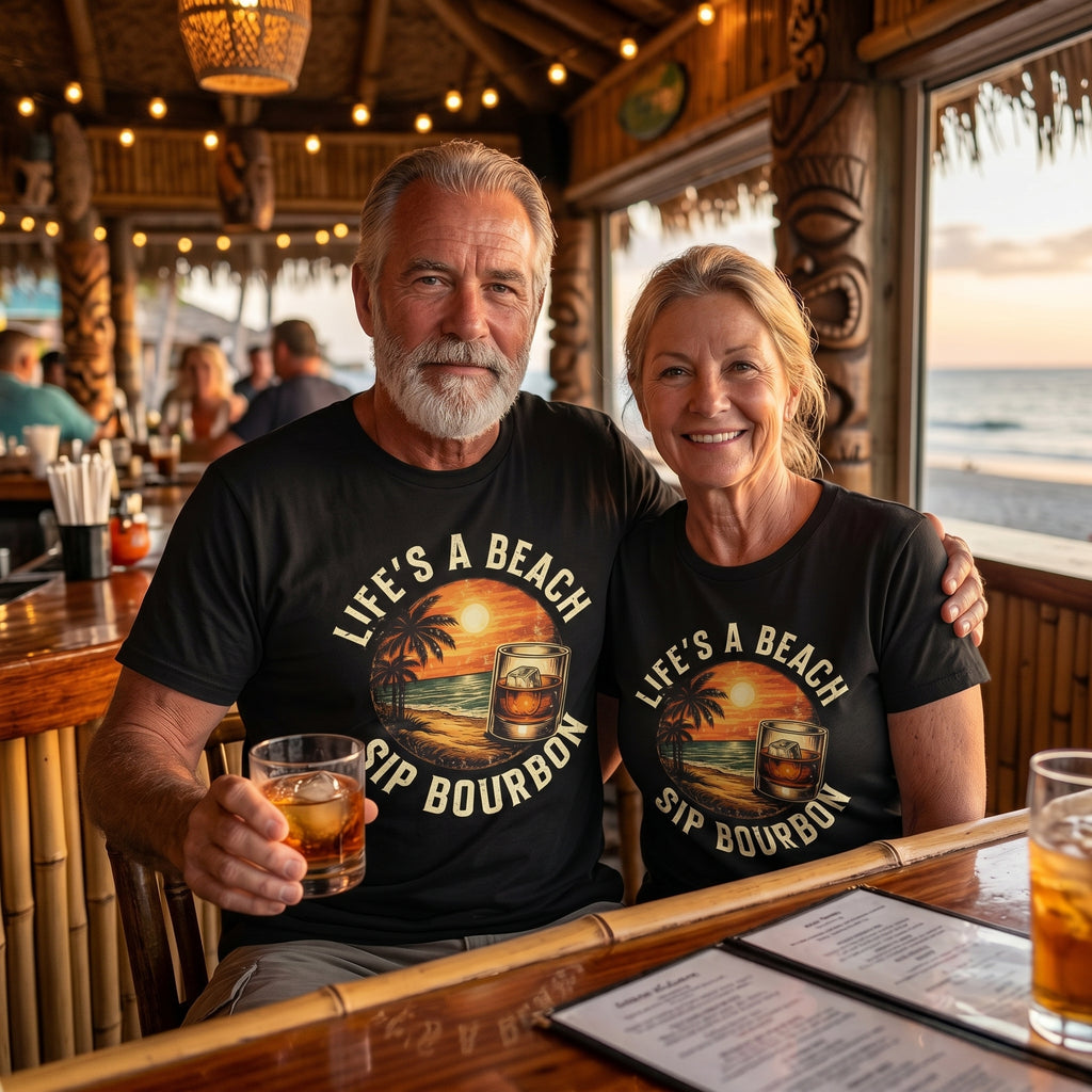 Man and woman wearing matching 'Life's a Beach, Sip Bourbon' shirts in a bar setting with ocean view.