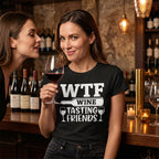 Two women in a bar setting with one holding a glass of wine and wearing a 'WTF Wine Tasting Friends' shirt.
