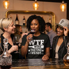 Three women at a bar enjoying wine, with one wearing a 'WTF Wine Tasting Friends' shirt.